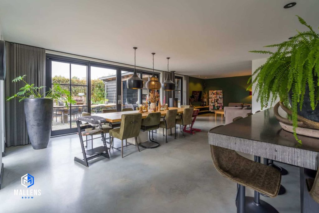 De vrijstaande woning in Biezenmortel vanbinnen. Je ziet de eethoek met een lange eettafel de voor de serre deuren staat. Er staat een grote bloempot naast de deuren.