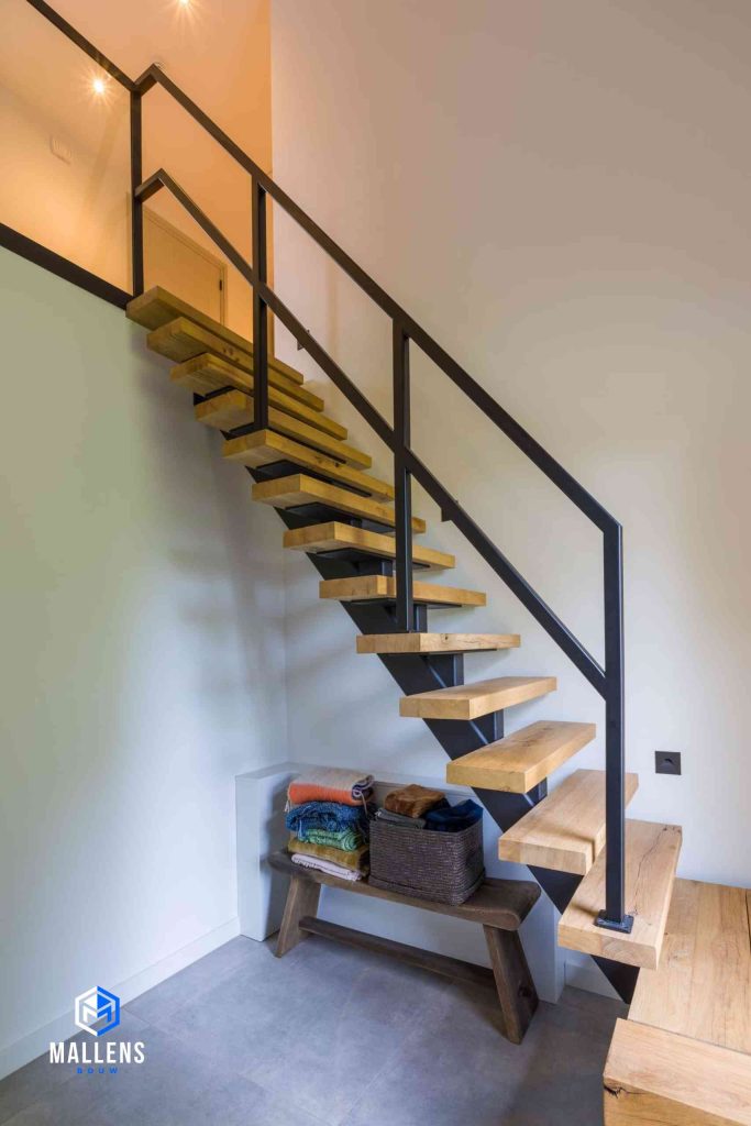 De trap van de woning. Het is een houten open trap met zwart staal. Onder de trap staat een bankje.