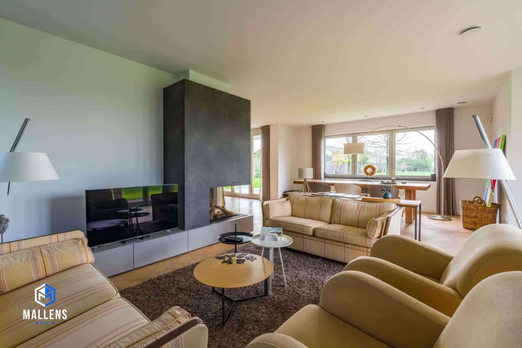 De zithoek met de tv, kachel, twee banken en 2 loungestoelen. Op de achtergrond zie je de eethoek.