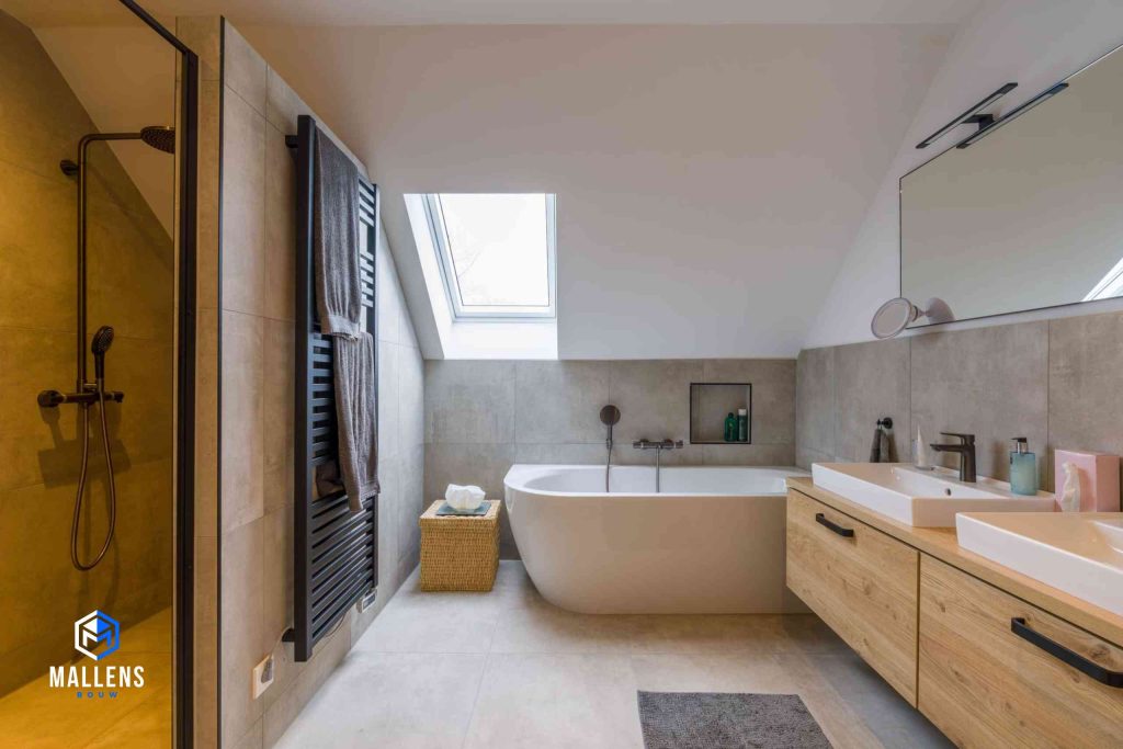 De badkamer van de woning met een groot ligbad, twee wasbakken en links zit een muurtje met daarachter de douches.