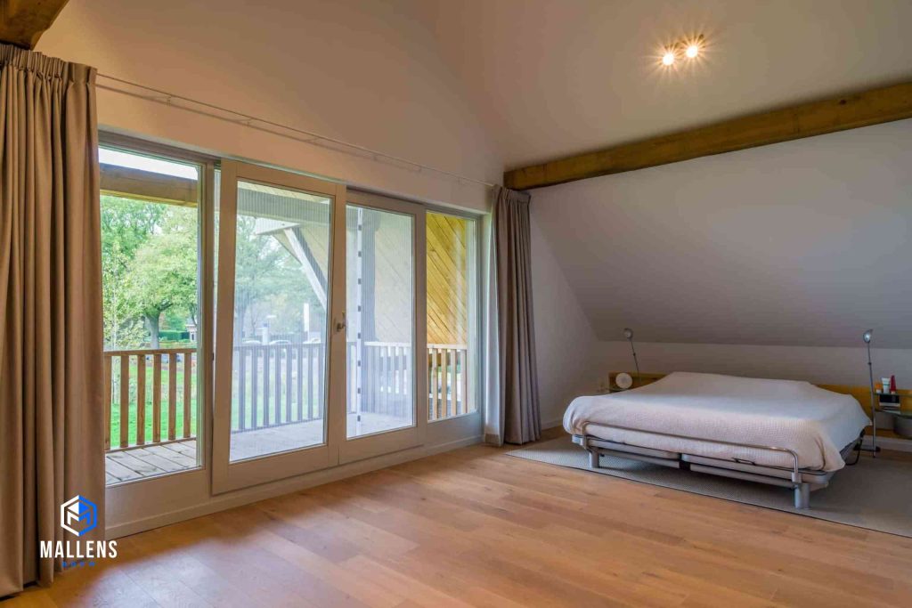 Een andere hoek van de slaapkamer. De kamer heeft een balkon en grote ramen en een deur.