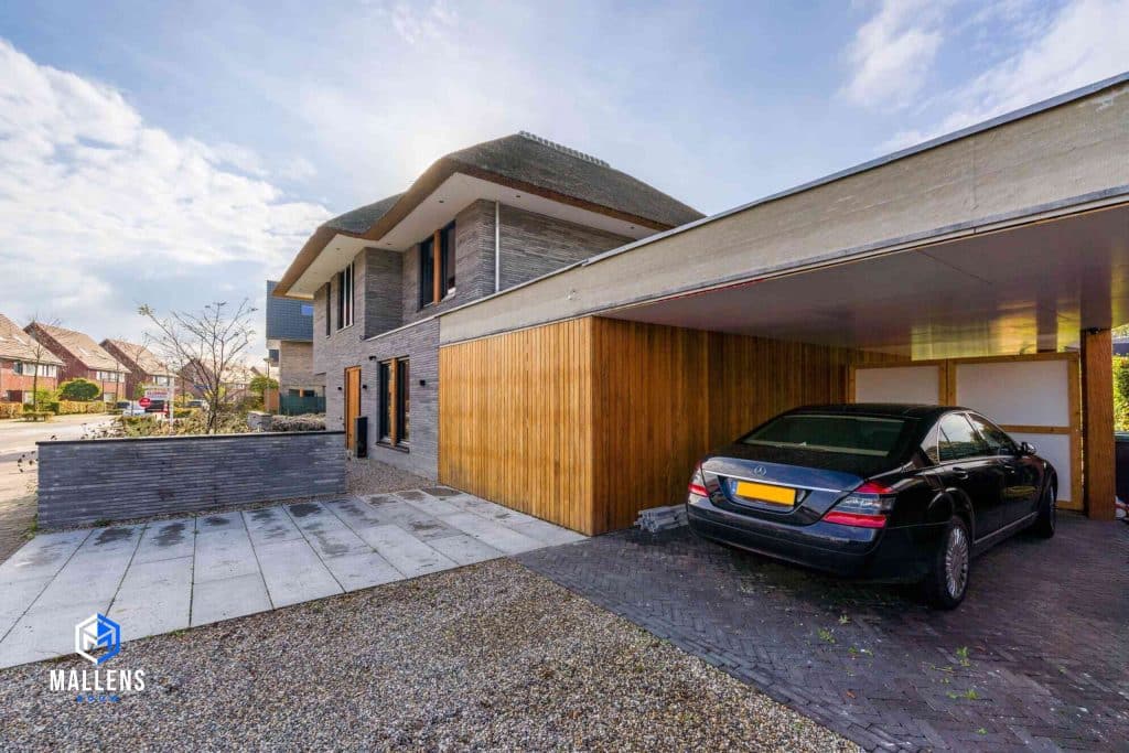 De houten schuur van de woning met daarnaast een overdekte plek voor de auto.