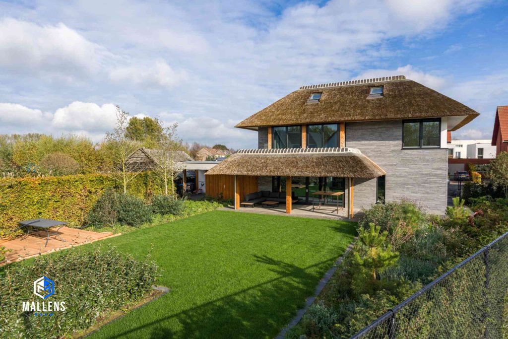 De moderne villa van de achterzijde bekeken. De woning heeft een overkapping met rieten dak en daaronder een zitplek.