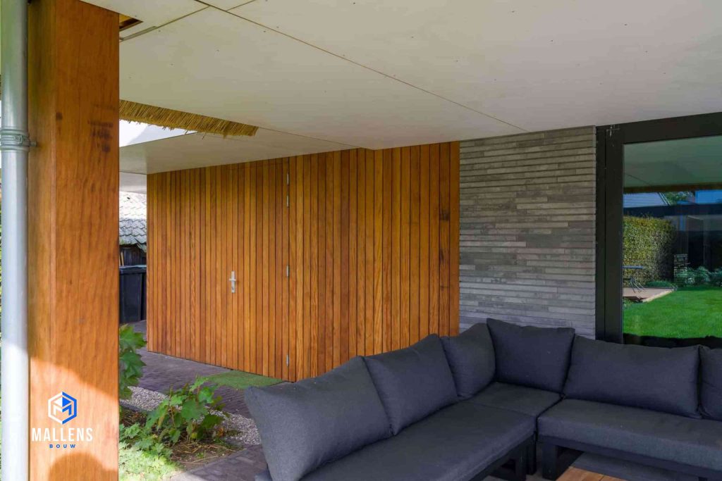 Het zitje in de de achtertuin onder de overkapping met de houten garagedeuren.