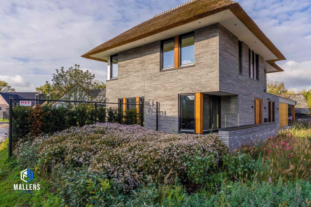 De vrijstaande moderne villa met rieten dak en grijze stenen.
