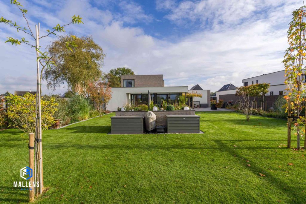De achtertuin van de woning met op de achtergrond de woning. In het midden van de tuin staat een verhoogde tuin met stenen muur en daarvoor twee kisten.