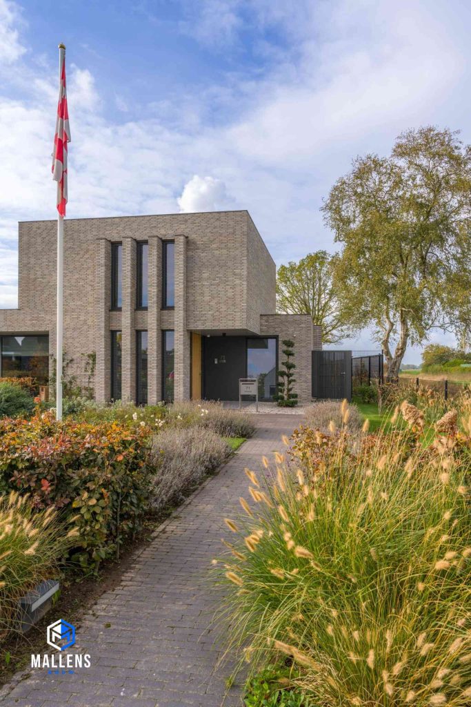 De woning van voren gezien, met een stuk van de voortuin, waar veel bloemen en planten in staan.