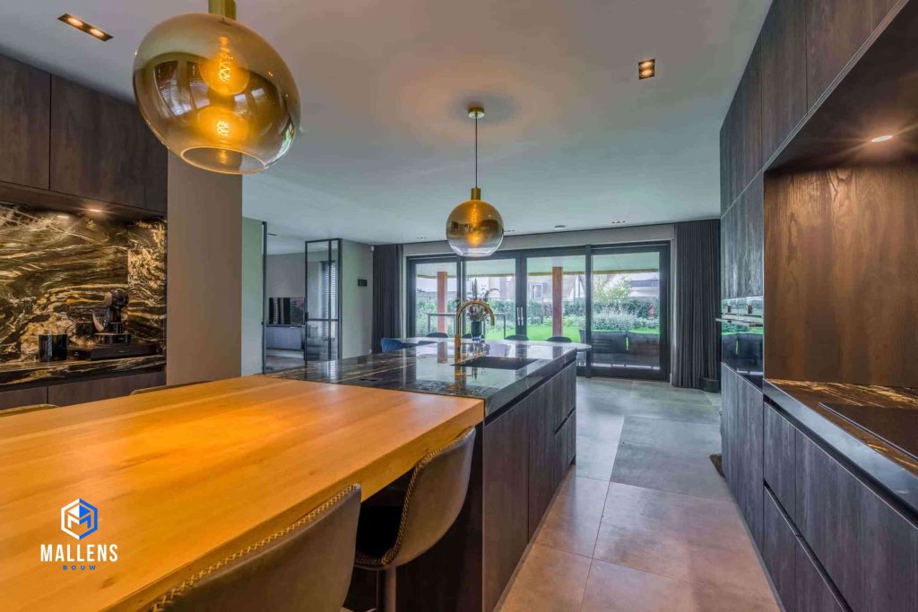 De keuken vanuit een andere hoek. Je ziet nu dat het keukenblok een houten gedeelte heeft waar de barkrukken aan staan. Op de achtergrond zie je de eethoek en de pui.