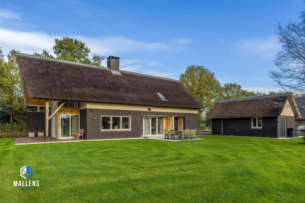 De woning vanaf de zijkant gezien. Je ziet de tuin met gras en een schuurtje. Ook in de zijkant zijn grote glazen deuren aanwezig.
