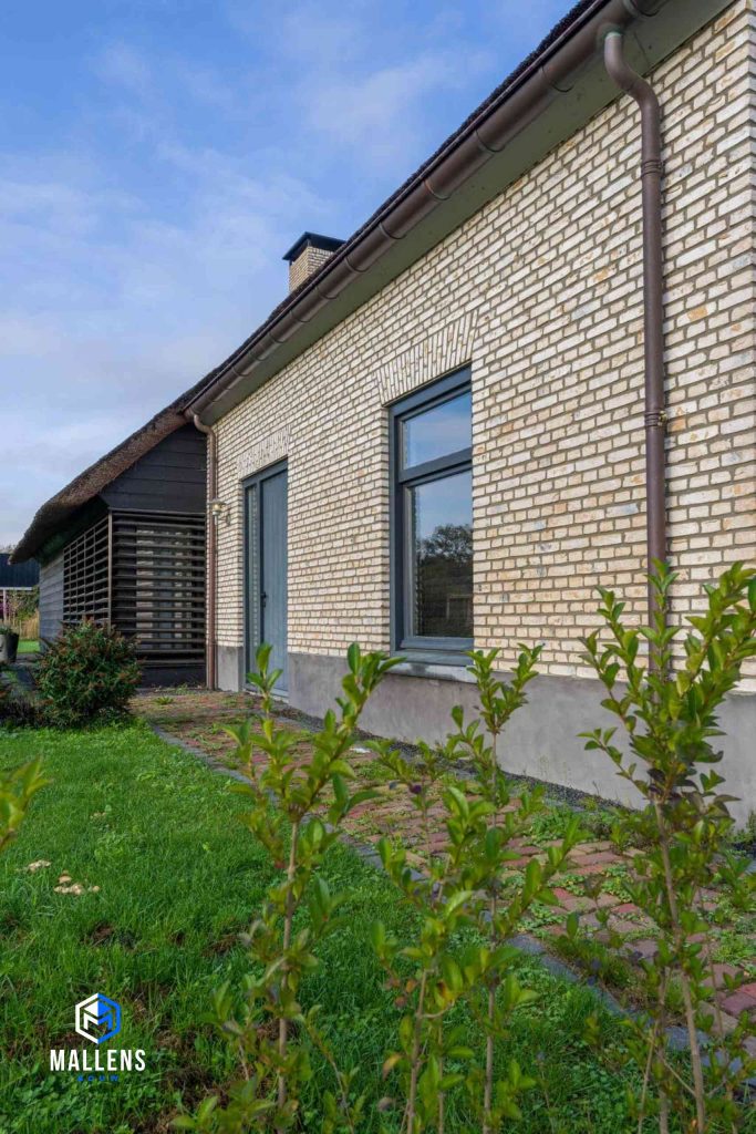 De gemetselde muur met voordeur en de betimmerde zwarte muur daarnaast.