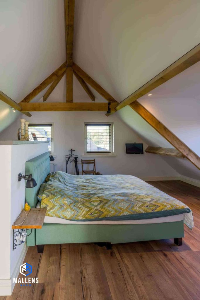 De slaapkamer met een tweepersoonsbed. Het dak loopt af in een punt en er zijn houten balken op het plafond verwerkt.
