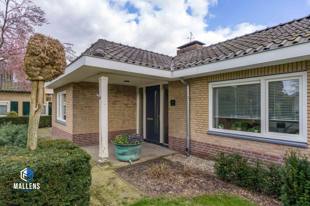 Je ziet de voorkant van de bungalow met de uitbouw en overkapping boven de voordeur.