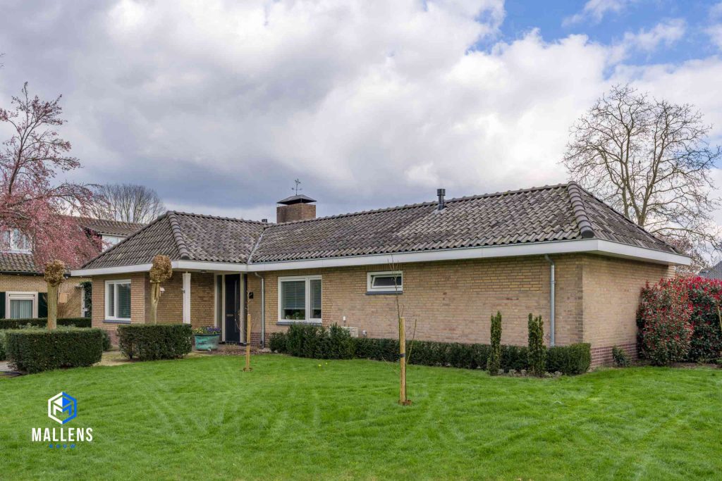 Je ziet de woning schuin van voren met het groene grasveld en struiken daarvoor.