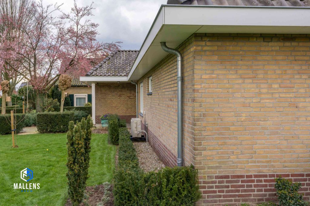 Je ziet de muur van de voorkant schuin gezien, met een regenpijp eraan en duidelijk beeld van het dakoverstek
