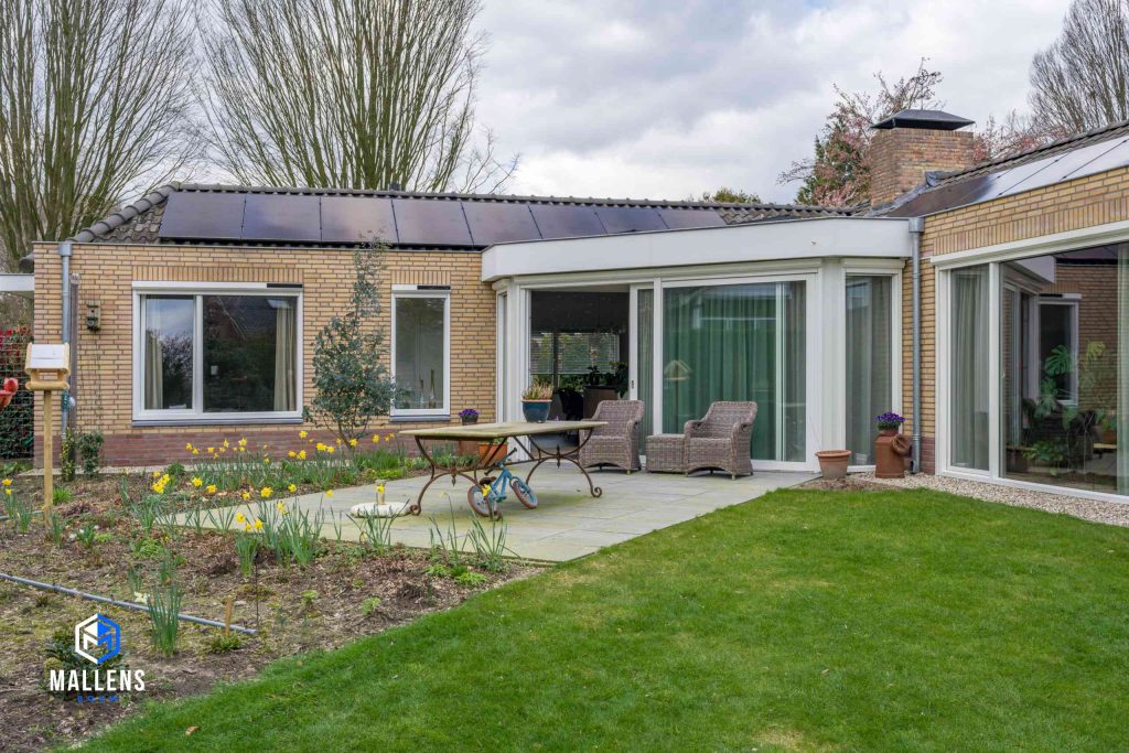 De achterzijde van de bungalow met een terrasje. Er liggen zonnepanelen op het dak.