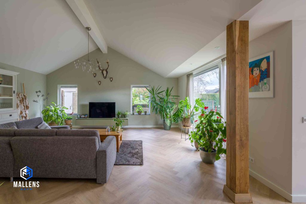 De woonkamer van achter gezien. Je kijkt op de achterkant van een gestoffeerde grijze bank en je ziet tegen de muur een tv staan.