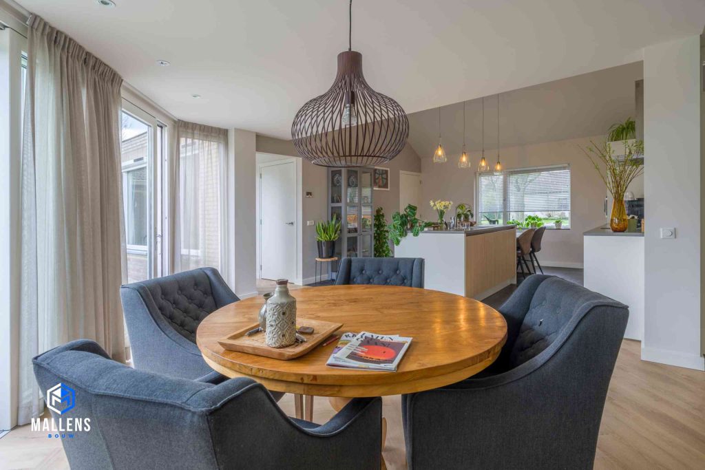 De ronde, houten eettafel met vier grijze gestoffeerde stoelen eromheen en op de achtergrond de keuken.