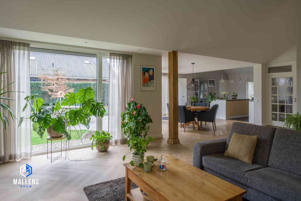 Een gedeelte van de woonkamer met diverse planten en uitzicht op de keuken.