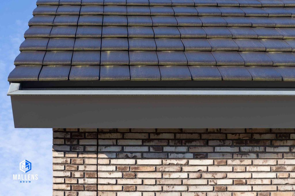 Detailfoto van het zwarte dak met de grijze dakgoot en een gedeelte van de in kleur wisselende bakstenen.