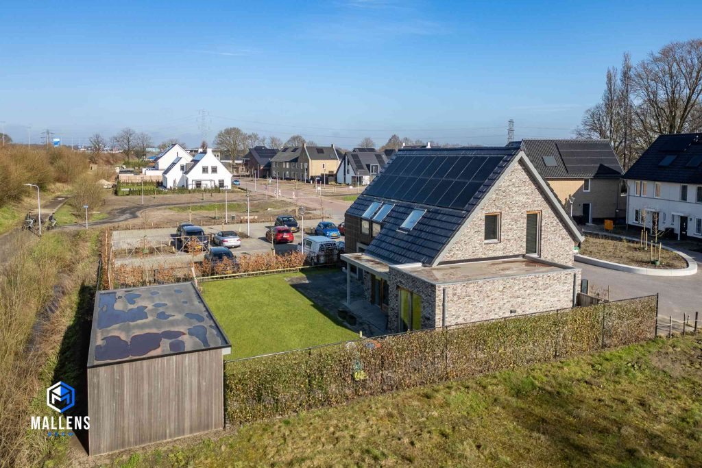 De woning van schuin achteren bezien, met zicht op de uitbouw, en de achtertuin met het groene gras.