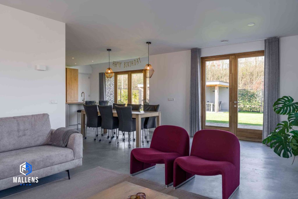 Een gedeelte van de woonkamer met een gestoffeerde bank en twee bordeauxrode loungestoelen. Je hebt vanuit de woonkamer zicht op de eettafel.
