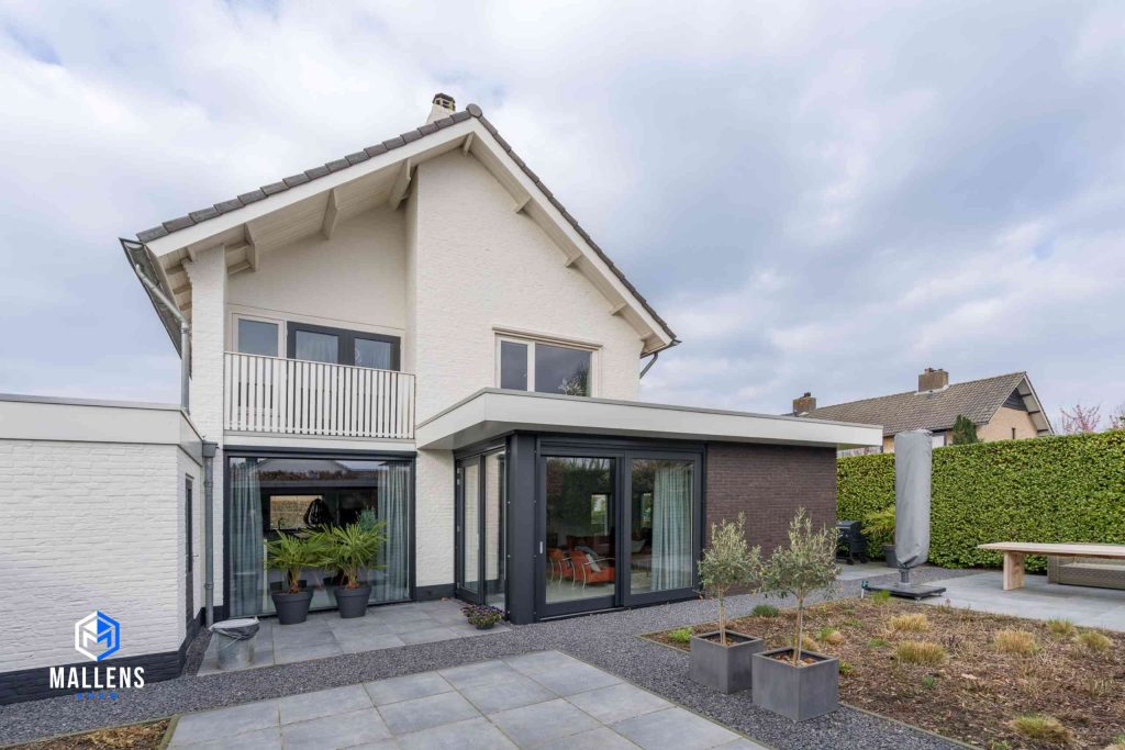 De woning met de uitbouw van schuin achter bekeken. De woning heeft een balkon en beneden zijn er ruime ramen aanwezig.