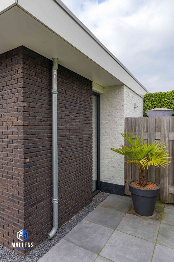 De muur van de uitbouw van dichtbij bezien, met een regenpijp voor de afvoer van het water van het platte dak.