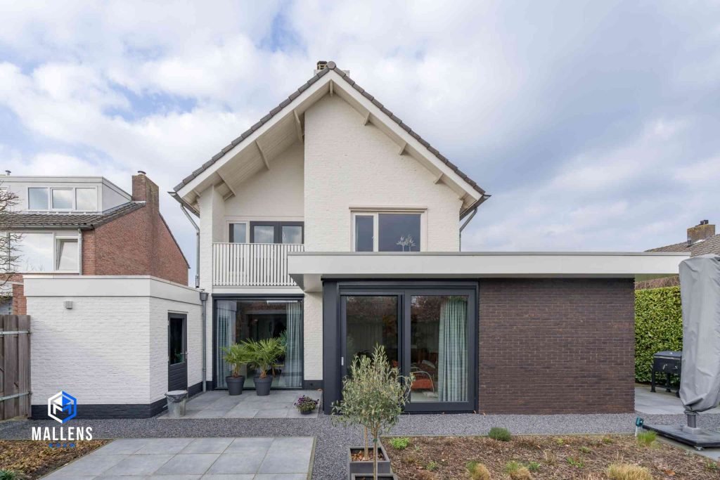 De witte woning van achteren bezien met de bruine uitbouw.
