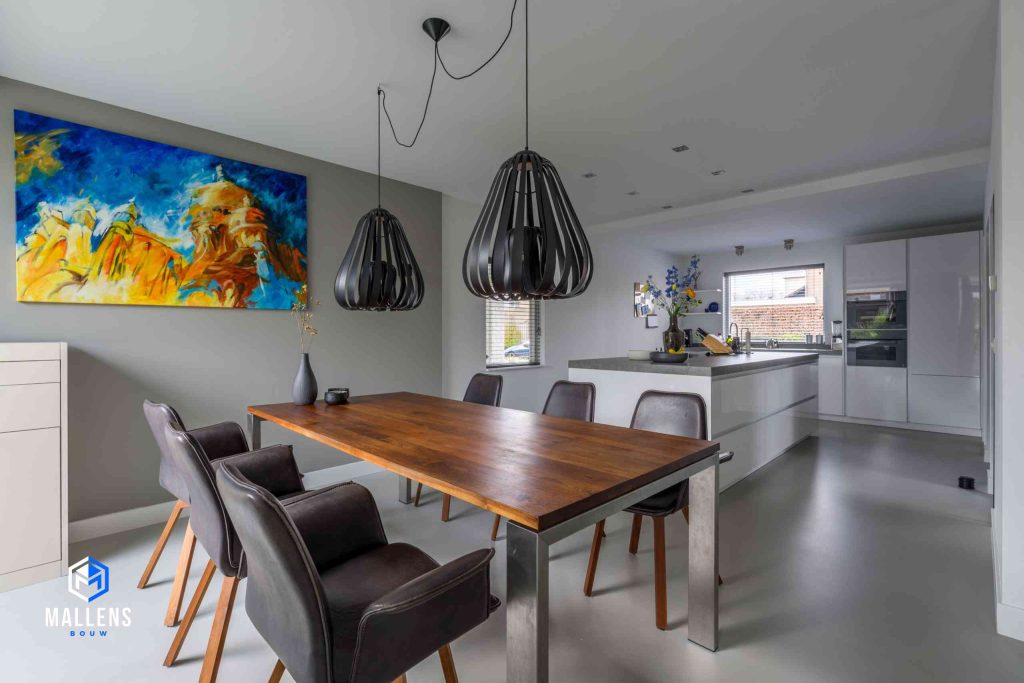 De eethoek van de woning met 6 zwarte leren stoelen. Op de achtergrond zie je de keuken en links hangt een kleurrijk schilderij op de muur.