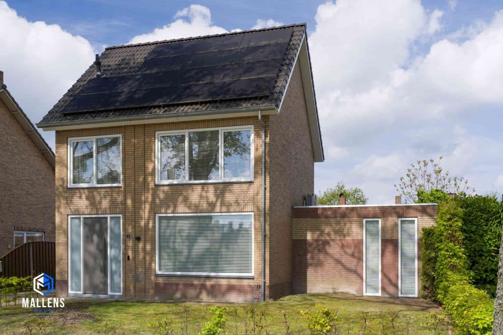 Woning Udenhout van schuin voren bekeken. Het is een vierkante woning met een aanbouw rechts.