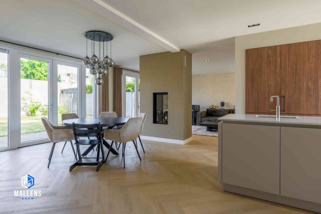 Je ziet de eethoek met ronde tafel met uitzicht op de achtertuin door de grote serredeuren.