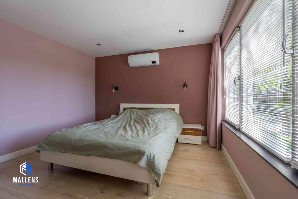Een roze slaapkamer met veel lichtinval vanuit de ramen.