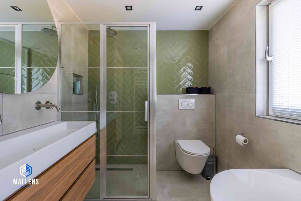 De badkamer met een zwevend toilet en ruim bad. Links is de wasbak met een grote ronde spiegel.