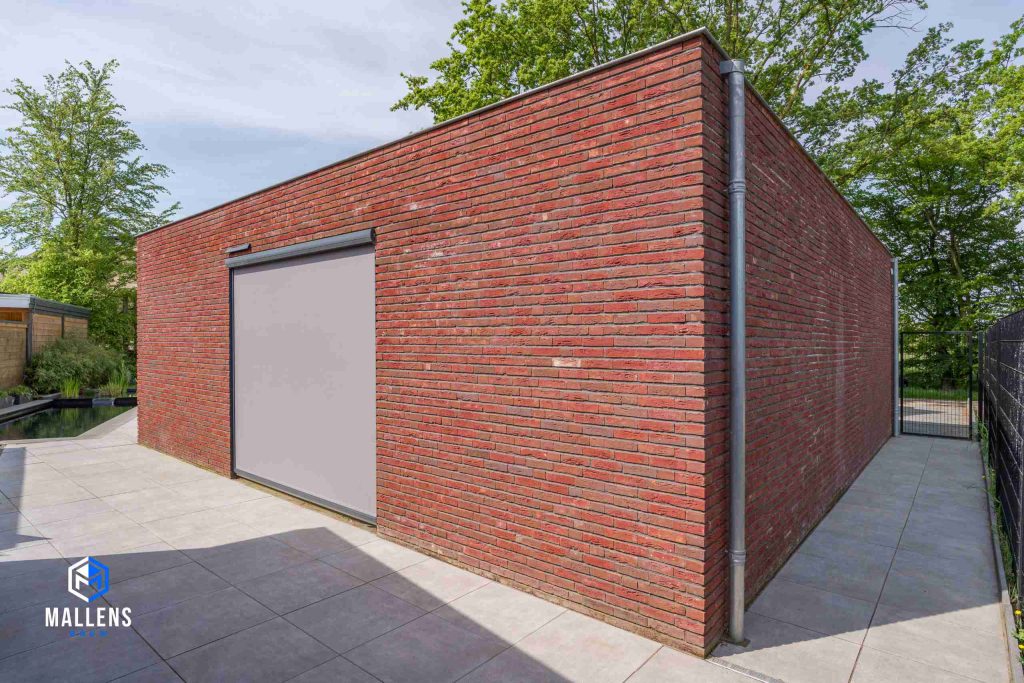 De garage, geheel in rode bakstenen, met een groot raam erin.