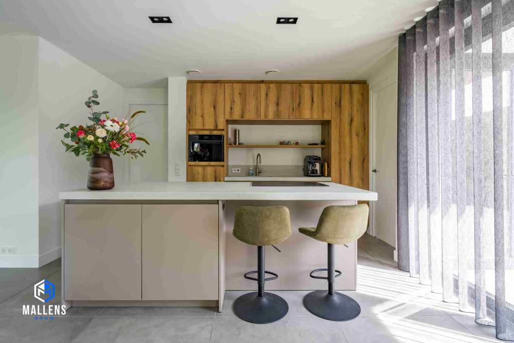De keuken met het keukenblok en 2 barstoelen daaraan. Op het keukenblok staat een grote vaas met bloemen.